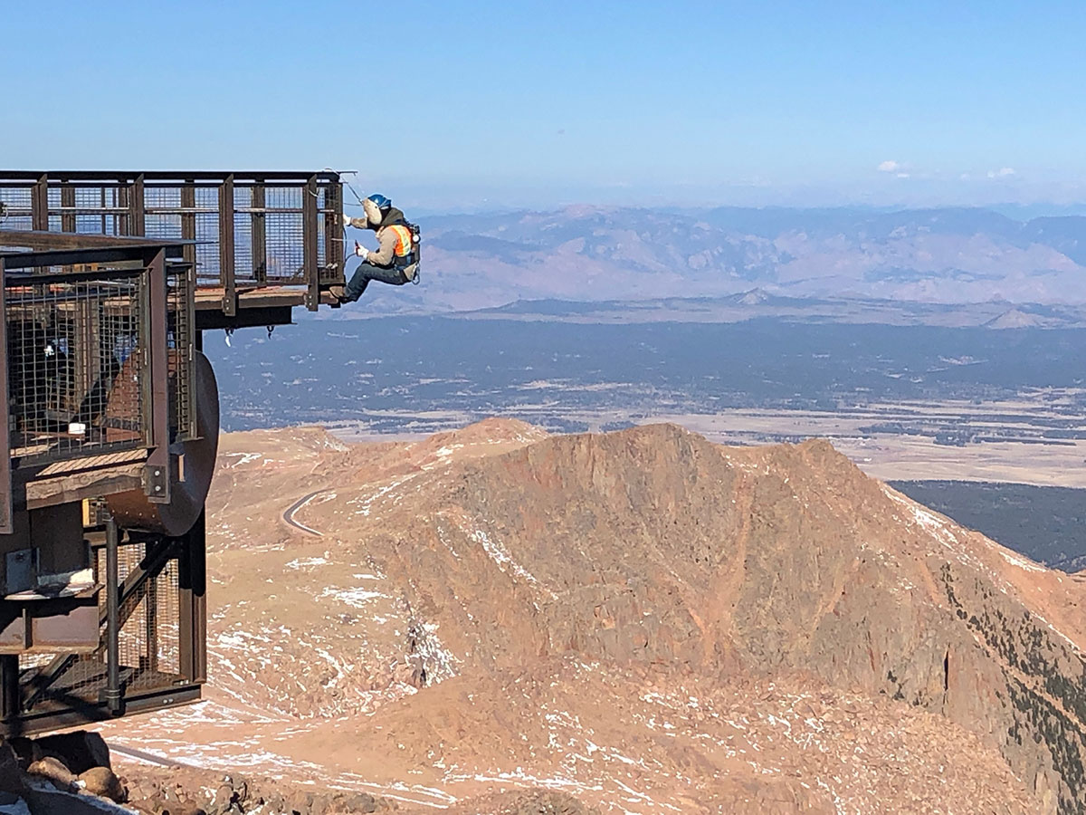 Pikes Peak Summit Complex engineer hangs off PermaTrak boardwalk over the Rocky Mountains